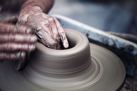 Hands working on pottery wheel , close up retro style toned photo wit shallow DOF