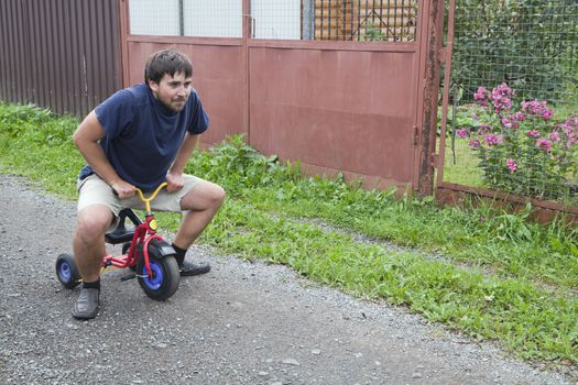 Adult man tying to ride on a small tricycle