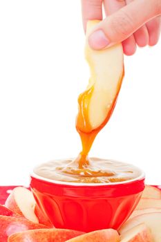 A slice of fresh apple being dipped into smooth, buttery caramel dip.  Shot on white background.