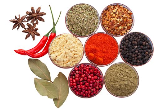 Tiny spices bowls along with loose star anise, bay leaves, & hot red peppers isolated on white.  Includes: oregano, red chilies, whole black pepper, sage, whole red pepper, garlic powder, and paprika.