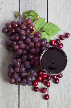 A glass of fresh cranberry grape juice surrounded by fresh cranberries and grapes.