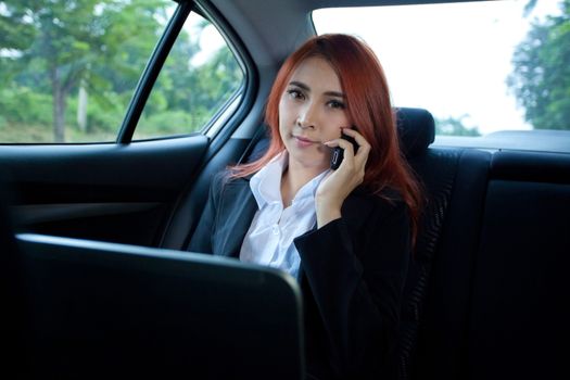 Beautiful young business asian woman using laptop and mobile phone in a car