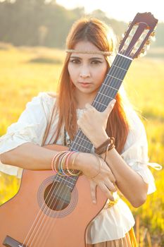 Hippie woman in golden field with acoustic guitar