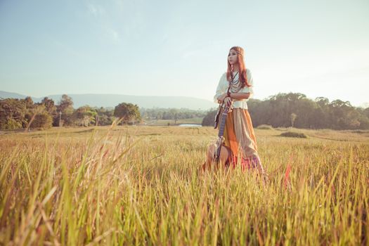 Hippie woman in golden field with acoustic guitar