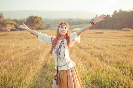 Hippie woman with arms outstretched in golden field on sunset