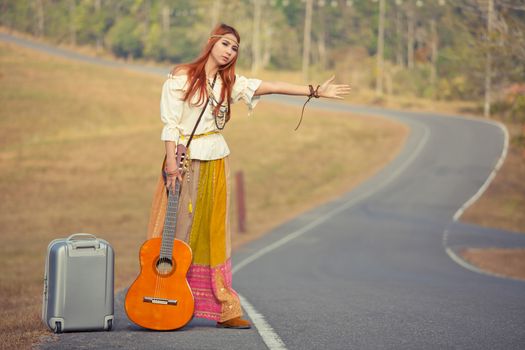 Hippie girl with guitar hitchhiking on countryside road