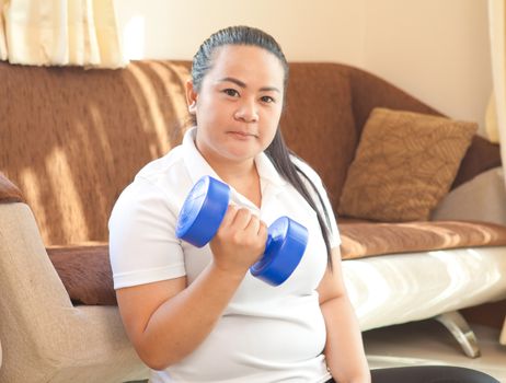 Young asian fat woman does fitness with dumbbell in home