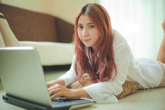 Happy asian young woman lying using laptop at home