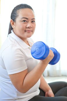 Young asian fat woman does fitness with dumbbell in home