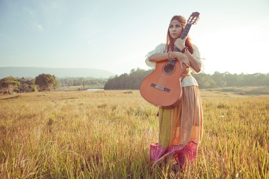 Hippie woman in golden field with acoustic guitar