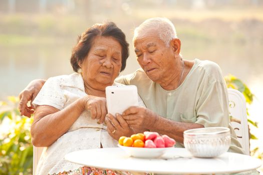 Happy asian senior couple using the tablet on outdoor background