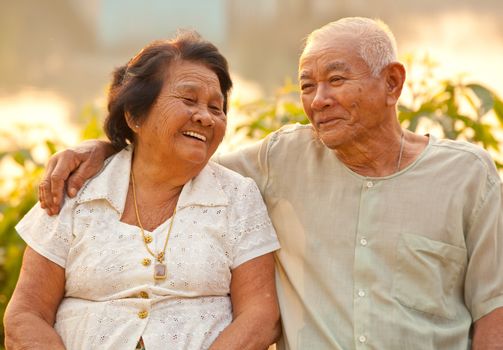 Happy Asian Senior couple sitting outdoors on sunset