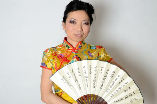 Elegant Chinese lady wearing traditional colorful dress. Kind female model from Asia holding fan in her hand. 