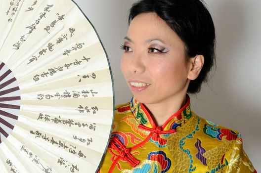 Elegant Chinese lady wearing traditional colorful dress. Kind female model from Asia holding fan in her hand. 