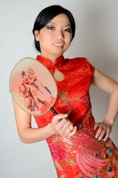 Elegant Chinese lady wearing traditional red dress. Pretty Asian female model holding fan in her hand. 