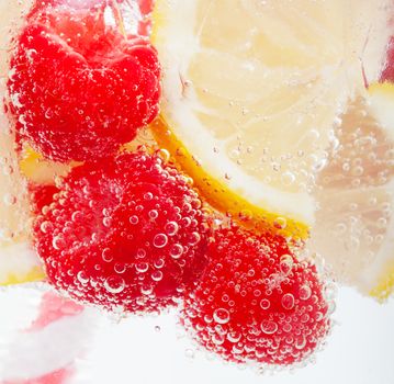 Raspberries and lemon slices in sparkling water.  Macro.  Focus on bubbles.