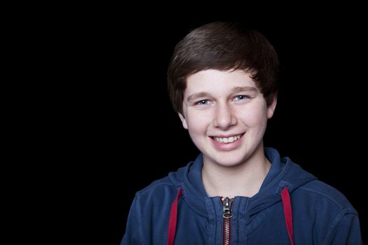 Portrait of a smiling fourteen year old boy on a black background.