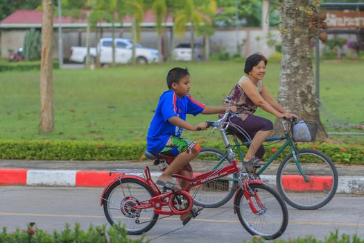 SURAT THANI, THAILAND - SEPTEMBER 22: Unidentified Thai senior woman and children riding bicycle in park on Sebtember 22, 2013 in Surat Thani, Thailand.