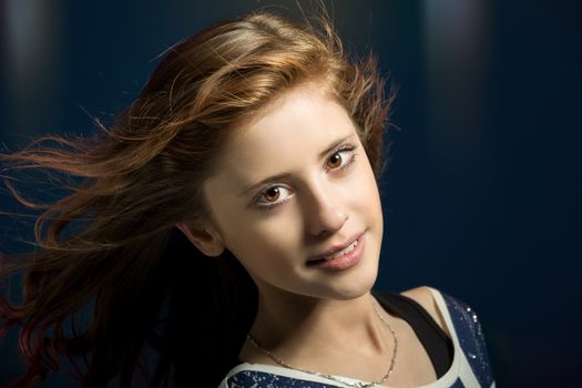 Studio fashion portrait of young beautiful girl with nice eyes on dark blue background with wind from fan in hair