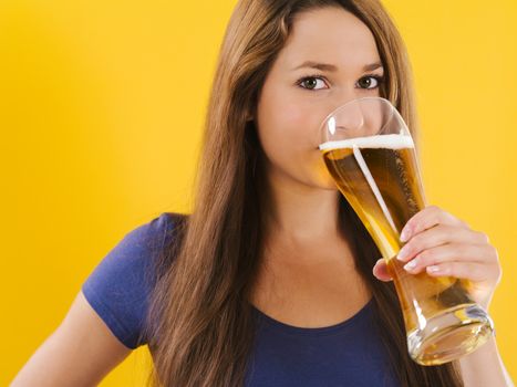 Photo of a beautiful young brunette woman drinking beer from a tall glass.