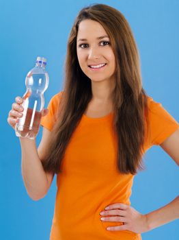 Photo of a beautiful young brunette woman drinking bottled water over blue background.