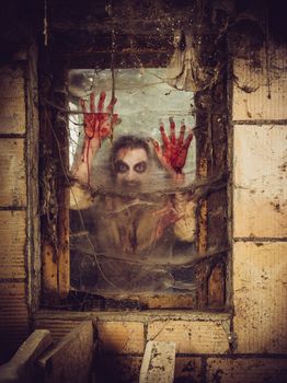 Photo of a zombie outside a window that is covered with blood, spiderwebs and filth.