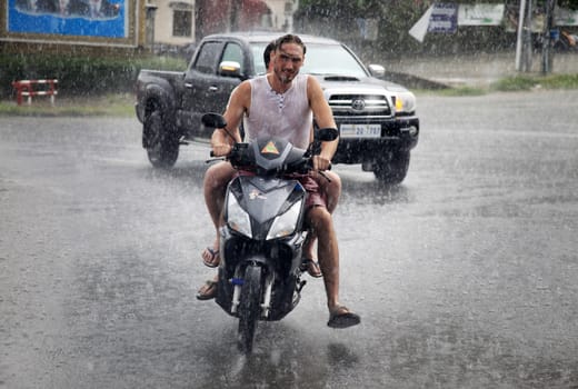 SIEM REAP, CAMBODIA - APRIL 18: Unidentified men on a motorcycle under the tropical rain in Siem Reap, Cambodia on the 18 April, 2014.