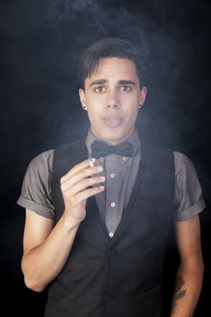 A young man holding a cigarette and blowing smoke straight at the camera.