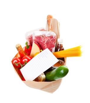 Wide angle view of a grocery bag full of barbecue staples with a hand written grocery list on top.