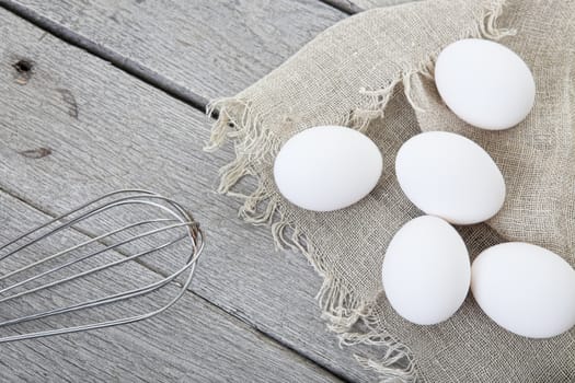 Eggs and whisk styled on a raw, aged wood background.
