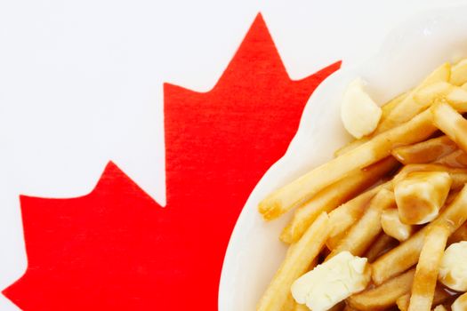 Poutine is a dish that people around the world associate with Canada.  Macro of poutine on a Canadian flag paper placemat.