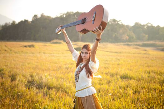 Hippie woman in golden field with acoustic guitar