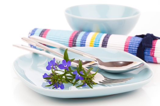 tableware with blue lobelia flowers and cutlery, on a white background.