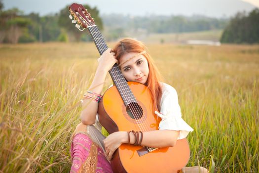 Pretty country hippie girl playing guitar on grass