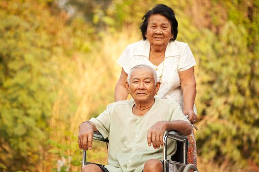 Asian senior woman pushing her disabled hasband on wheelchair