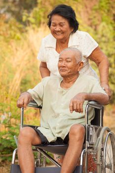 Asian senior woman pushing her disabled hasband on wheelchair