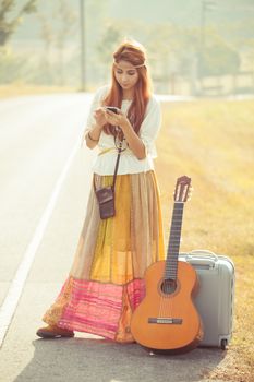 Beautiful young hippie girl using mobile phone on the country road