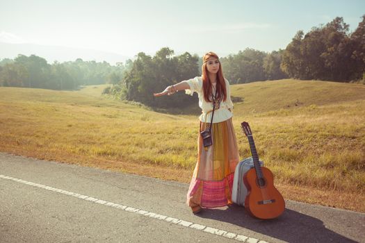 Hippie girl with guitar hitchhiking on countryside road