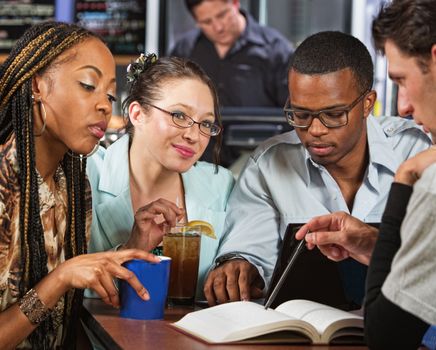 Cute group of four diverse students at table with book