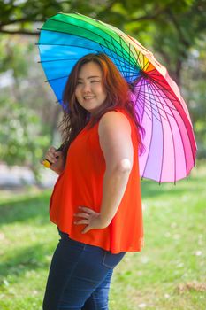 Happy fatty asian woman with umbrella outdoor in a park