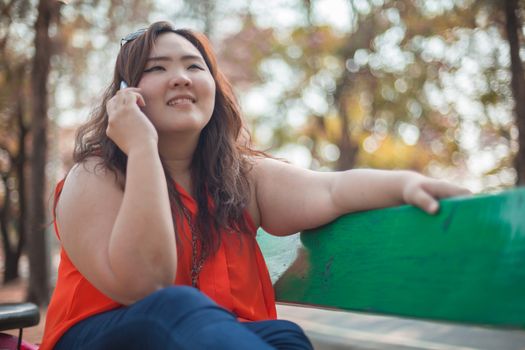 Happy fatty asian woman using mobile phone outdoor in a park