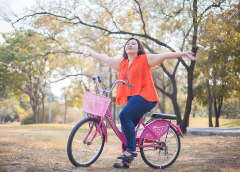 Happy fatty asian woman outstretched with bicycle outdoor in a park