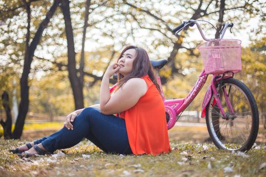 Happy fatty asian woman posing with bicycle outdoor in a park