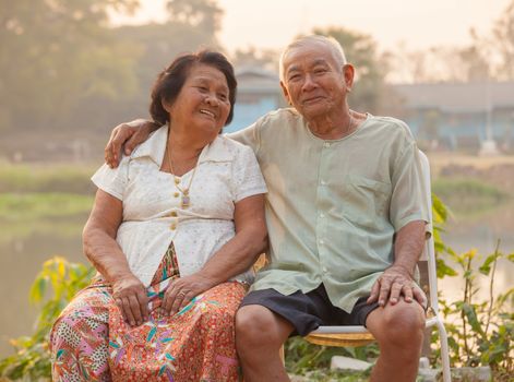 Happy Asian Senior couple sitting outdoors on sunset