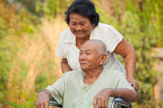 Asian senior woman pushing her disabled hasband on wheelchair