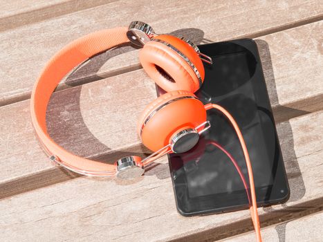 Vibrant orange headphones and black tablet pc on wooden bench for mobile language learning or distance education