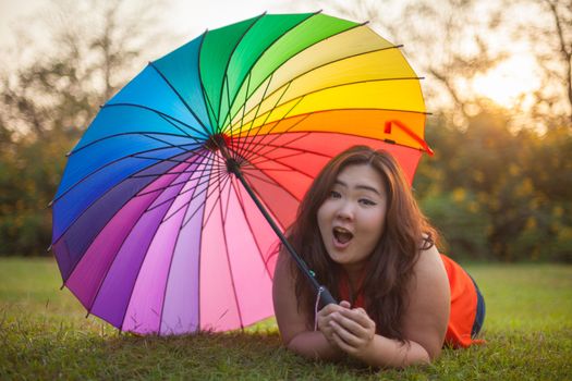 Happy fatty asian woman with umbrella outdoor in a park