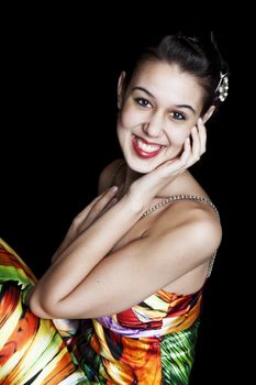 A young gir, with a huge smile,l dressed in a colorful prom gown.  Shot on black background.
