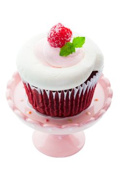 Red Velvet cupcake with pink and white whipped cream cheese icing, and a sugared raspberry with a sprig of mint as garnish.  Served on a mini cupcake pedestal.  Shot on white background.