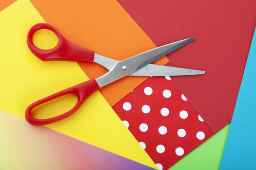 Different colored scrapbooking and construction paper with a pair of scissors on top.